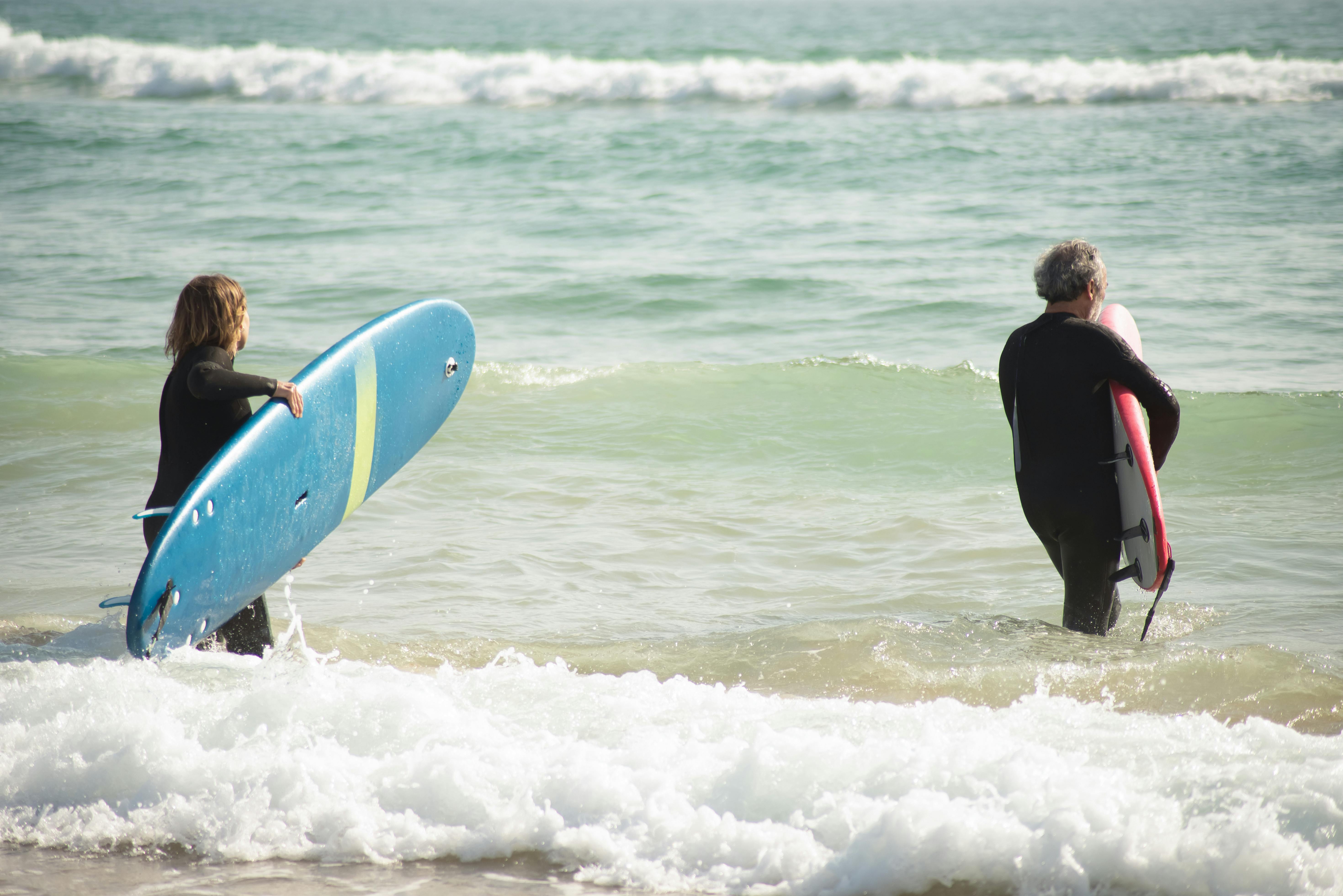 Two surfers walking into the ocean with surfboards during a Cape Town surf and hike day tour.